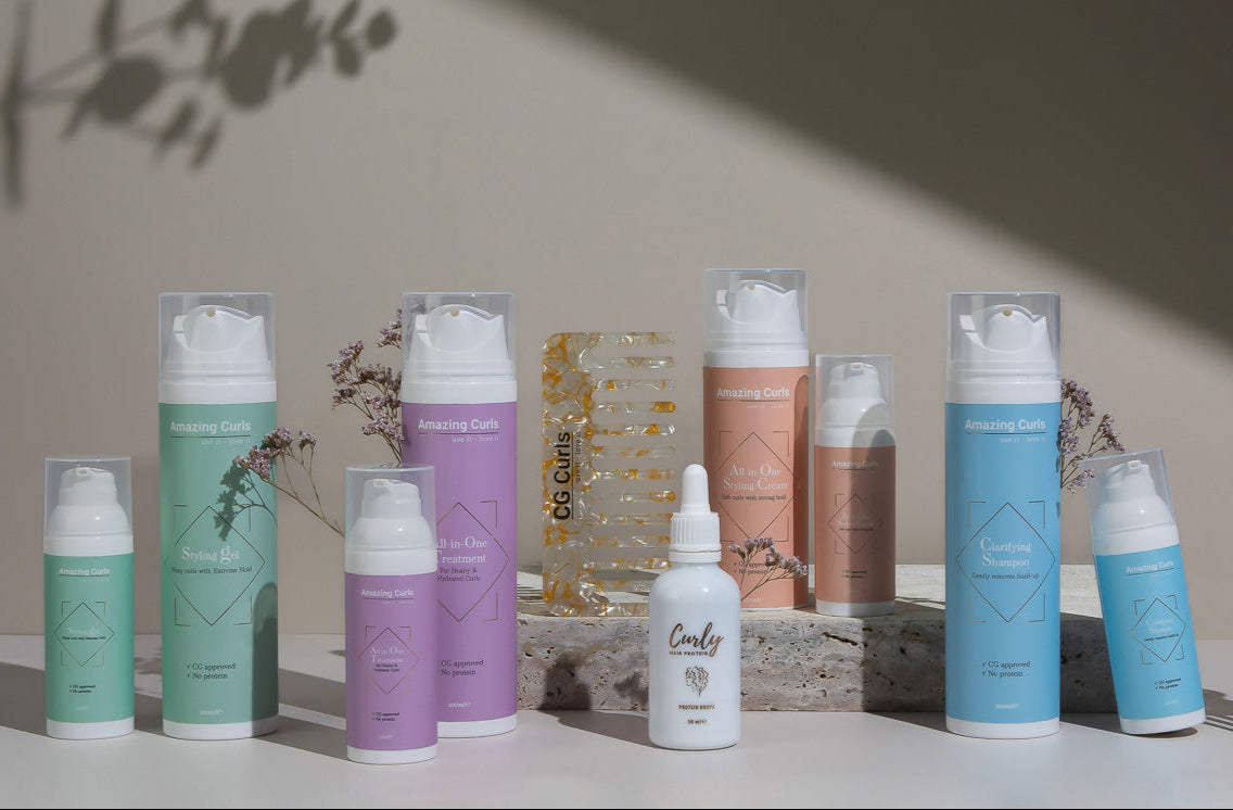 Diverse krullenproducten van Amazing Curls in pastelverpakkingen, opgesteld met decoratieve droogbloemen en glazen object.