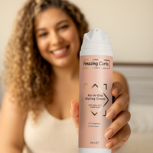 Vrouw met krullend haar die een fles All-in-One Styling Cream van Amazing Curls dicht bij de camera houdt.