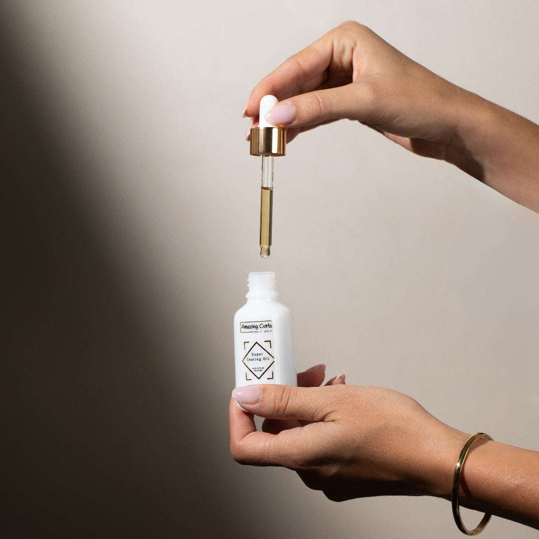 Hand met pipet boven open flesje Super Sealing Oil van Amazing Curls, krullenproducten voor krullendhaar en cgmethode